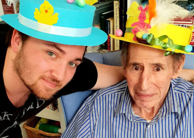 Male staff member and resident smiling at the camera wearing their home made Easter bonnets
