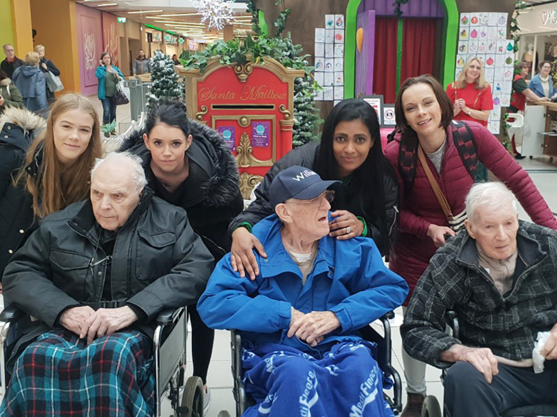 Three Lukestone Care Home residents in wheelchairs with staff, posing for a photo at the shopping Mall