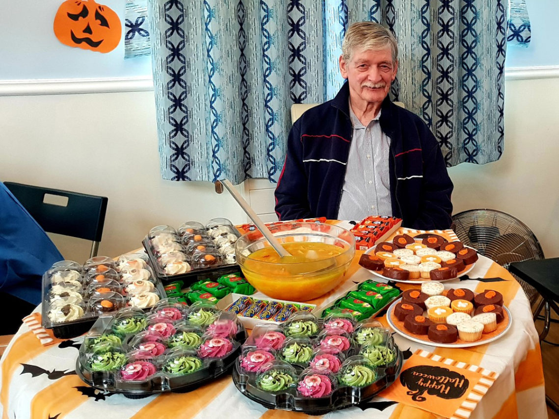 Lukestone Care Home resident sitting with a table of colourful Halloween cakes