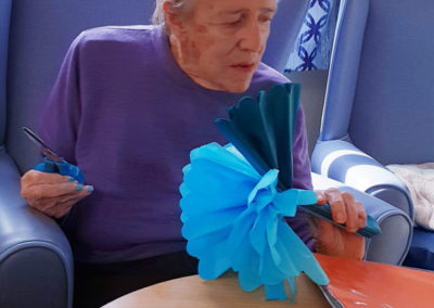 Female resident at Lulworth House making a blue tissue paper pom pom