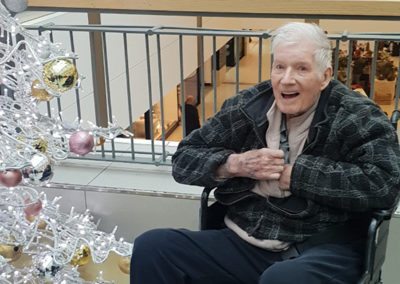 Lukestone Care Home resident sitting next to a festive Christmas tree at a shopping centre