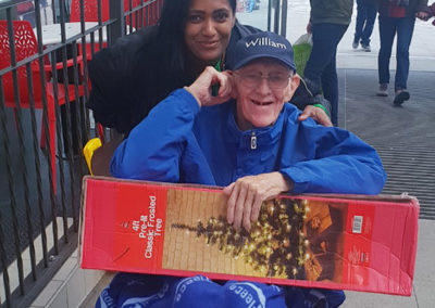 Lukestone Care Home male resident, with a member of staff, holding a newly purchased boxed Christmas tree at a shopping centre